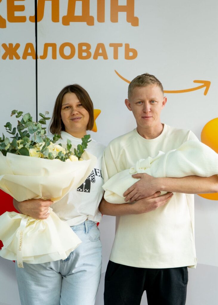 Фотосессия выписки из роддома в Алматы: папа держит младенца на руках у входа